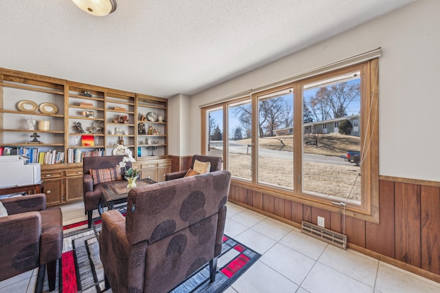 living room featuring wooden walls, visible vents, a textured ceiling, and wainscoting