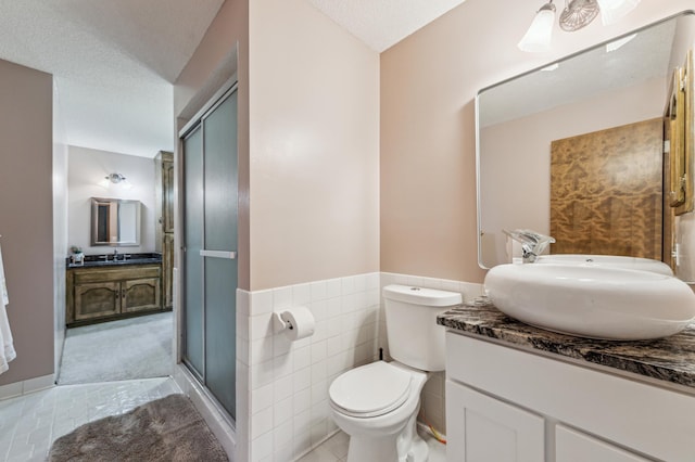 bathroom featuring a textured ceiling, toilet, vanity, tile patterned floors, and a stall shower