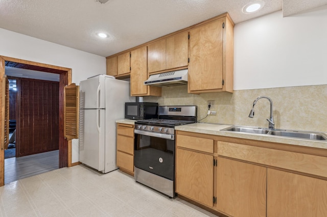 kitchen featuring freestanding refrigerator, a sink, black microwave, under cabinet range hood, and stainless steel gas range oven