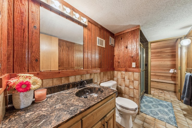 bathroom with a textured ceiling, toilet, wooden walls, visible vents, and a stall shower