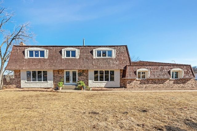 view of front of property featuring french doors, mansard roof, a front yard, and brick siding