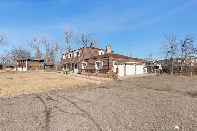 view of front of home featuring an attached garage, aphalt driveway, a chimney, and mansard roof