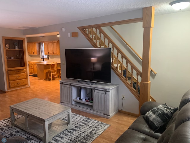 living room with stairs, a textured ceiling, and light wood-style flooring