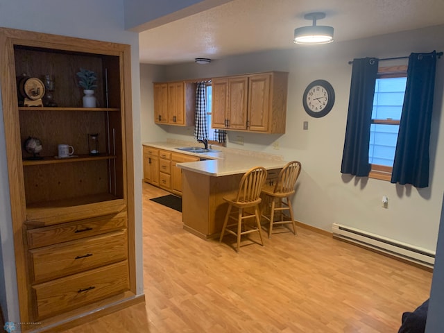 kitchen featuring a baseboard radiator, a breakfast bar, a sink, light countertops, and light wood-type flooring