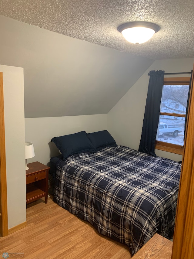 bedroom featuring a textured ceiling, vaulted ceiling, and light wood-type flooring