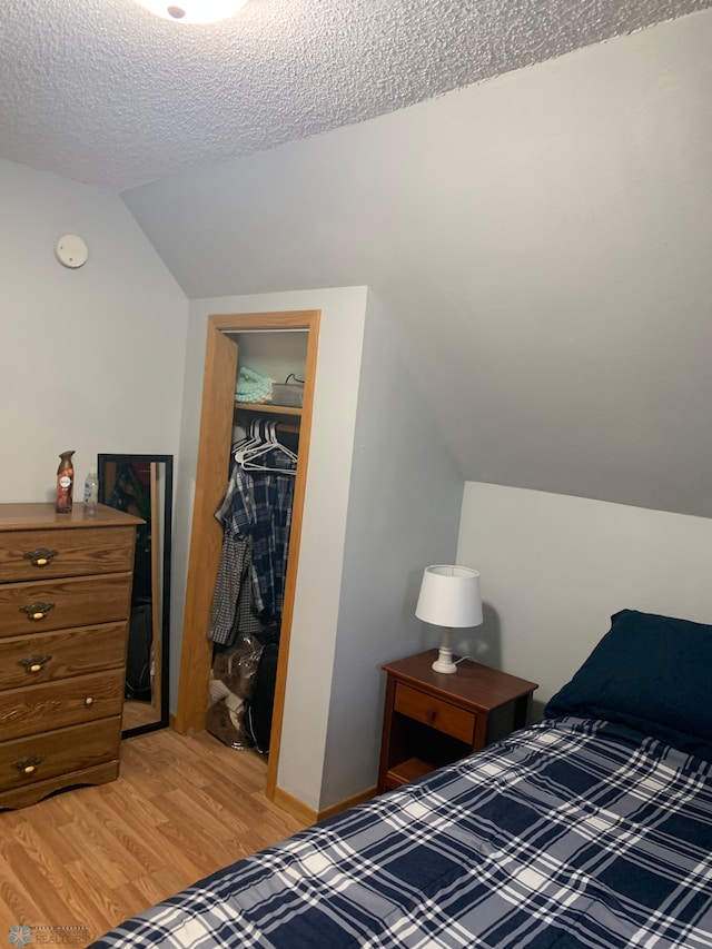 bedroom featuring baseboards, vaulted ceiling, a textured ceiling, light wood-type flooring, and a closet