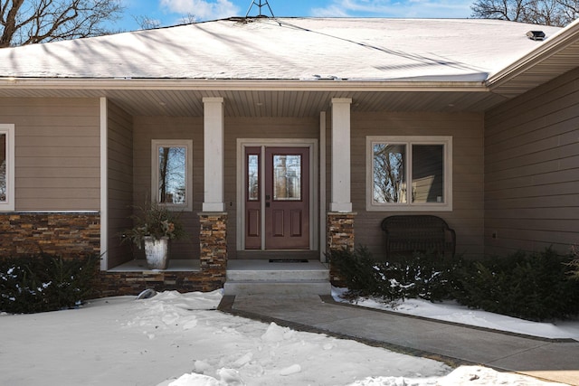 snow covered property entrance featuring covered porch and stone siding