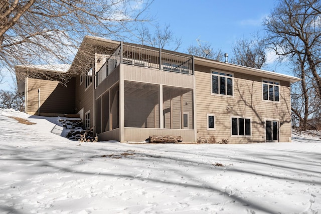 snow covered rear of property with a sunroom and a balcony