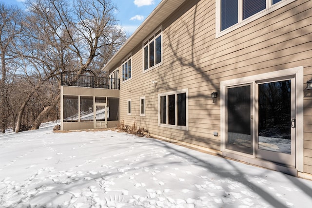 snow covered house featuring a balcony and a sunroom