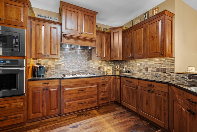 kitchen with dark wood finished floors, stainless steel microwave, oven, gas stovetop, and backsplash