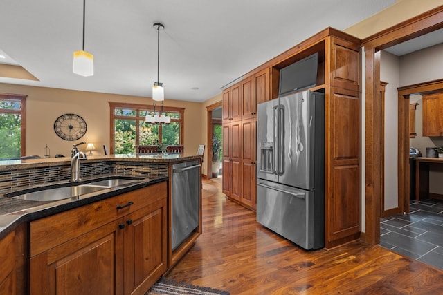 kitchen featuring pendant lighting, dark wood finished floors, appliances with stainless steel finishes, brown cabinetry, and a sink