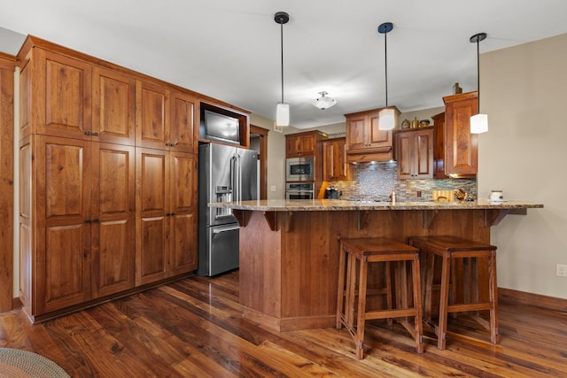 kitchen with brown cabinets, stainless steel appliances, backsplash, light stone countertops, and a peninsula