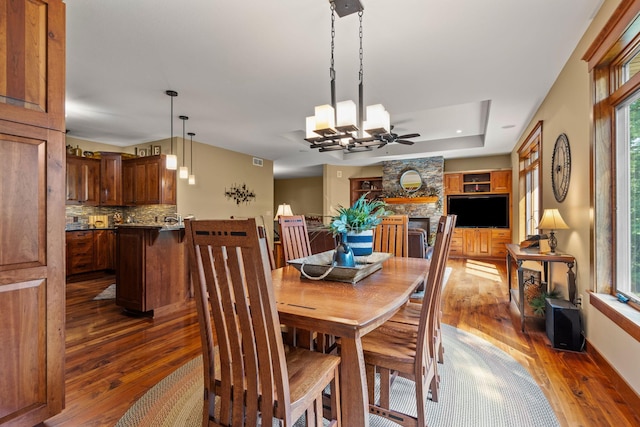 dining area featuring a tray ceiling, a stone fireplace, wood finished floors, and visible vents