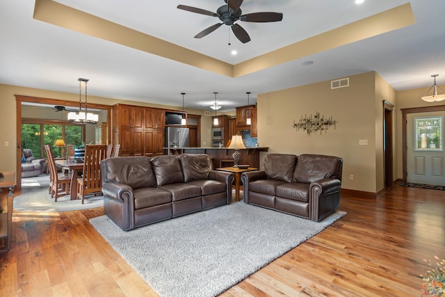 living area with a tray ceiling, visible vents, ceiling fan, wood finished floors, and baseboards