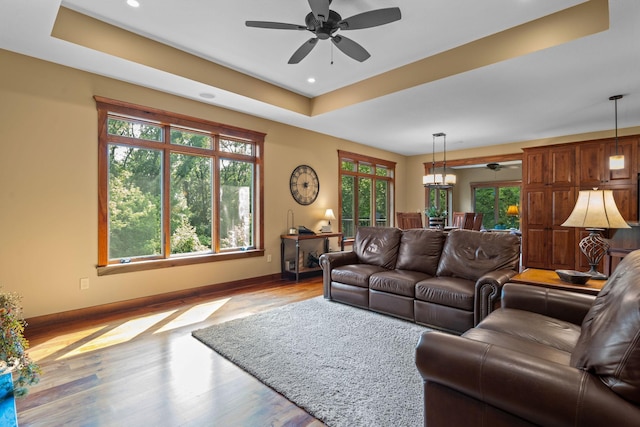 living room featuring ceiling fan, a tray ceiling, wood finished floors, and baseboards