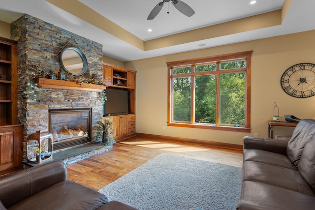 living area featuring light wood-style flooring, a fireplace, baseboards, and a raised ceiling