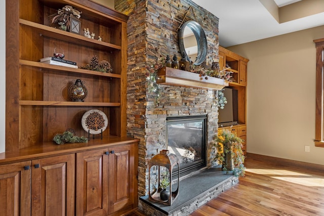 room details featuring a stone fireplace, wood finished floors, built in shelves, and baseboards