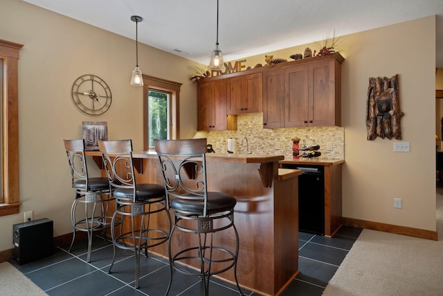 kitchen featuring a breakfast bar area, dark tile patterned flooring, light countertops, backsplash, and brown cabinetry