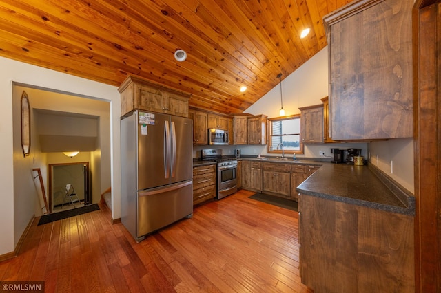 kitchen with appliances with stainless steel finishes, dark countertops, wood-type flooring, a sink, and high vaulted ceiling