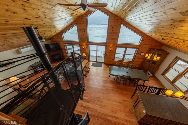living room with high vaulted ceiling, healthy amount of natural light, wooden walls, wooden ceiling, and a ceiling fan