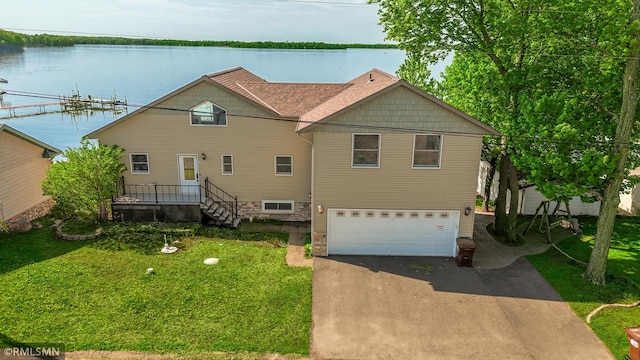 view of front of property with an attached garage, asphalt driveway, a water view, and a front lawn