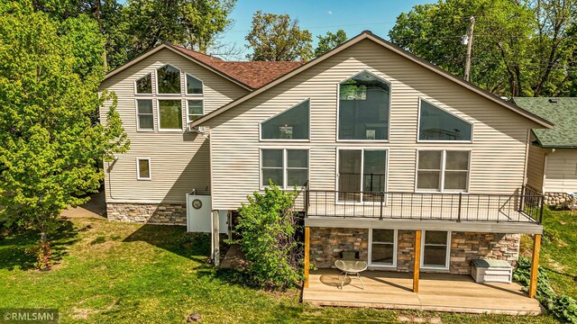 back of property featuring stone siding, a lawn, a balcony, and a shingled roof