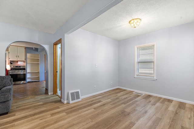 spare room featuring light wood-type flooring, arched walkways, visible vents, and baseboards