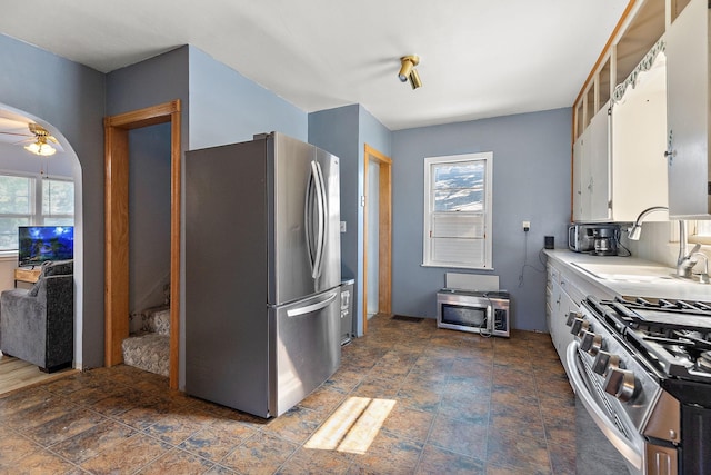 kitchen with stainless steel appliances, light countertops, a ceiling fan, white cabinetry, and a sink