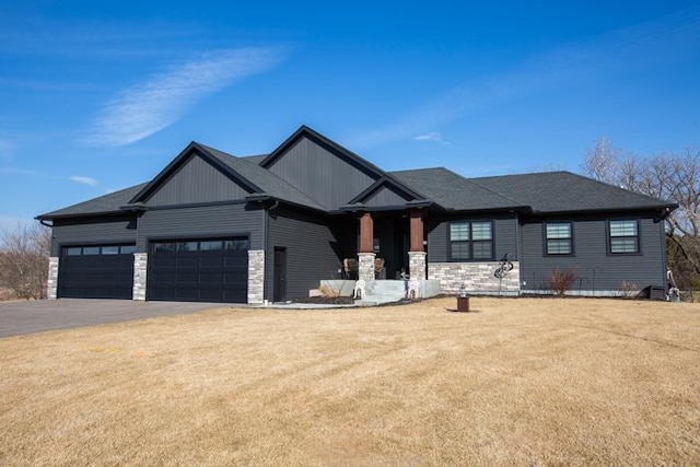 view of front of property featuring a front yard, a garage, stone siding, and driveway