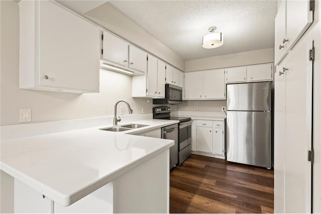 kitchen featuring dark wood-style floors, appliances with stainless steel finishes, a sink, a textured ceiling, and a peninsula