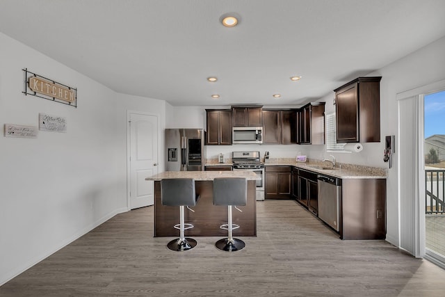 kitchen featuring appliances with stainless steel finishes, a center island, a sink, and dark brown cabinetry