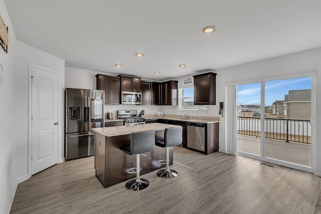 kitchen with dark brown cabinetry, light wood-style flooring, a breakfast bar, a center island, and stainless steel appliances