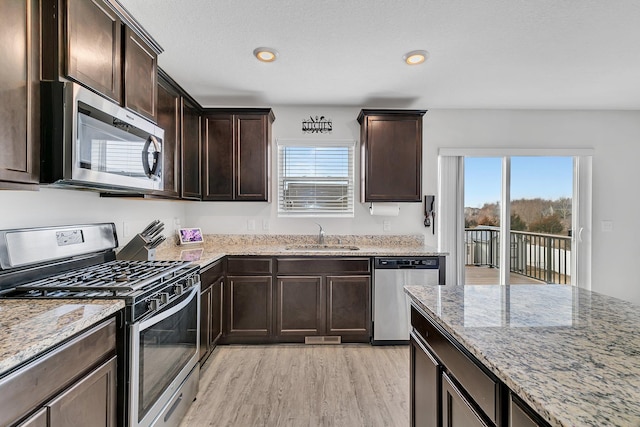 kitchen with stainless steel appliances, light wood-style floors, a sink, dark brown cabinetry, and light stone countertops