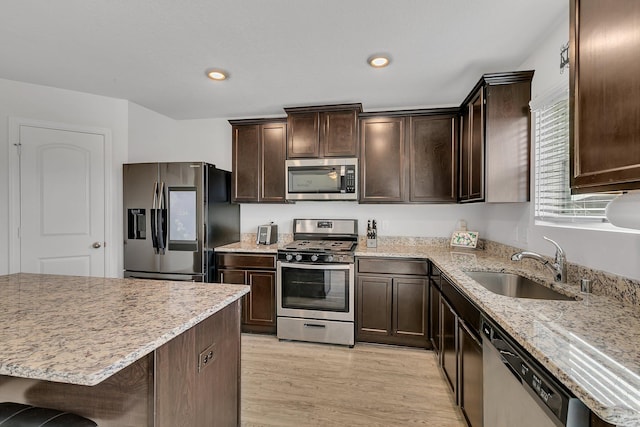 kitchen with dark brown cabinetry, appliances with stainless steel finishes, light stone counters, and a sink