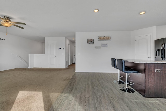 kitchen with recessed lighting, light stone counters, a kitchen breakfast bar, and stainless steel fridge with ice dispenser