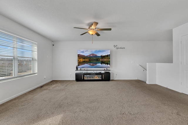 unfurnished living room featuring carpet floors, a glass covered fireplace, baseboards, and a ceiling fan