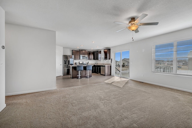 unfurnished living room with light carpet, baseboards, ceiling fan, a textured ceiling, and recessed lighting