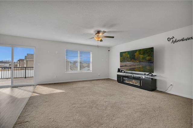 unfurnished living room featuring a textured ceiling, baseboards, a glass covered fireplace, and a healthy amount of sunlight