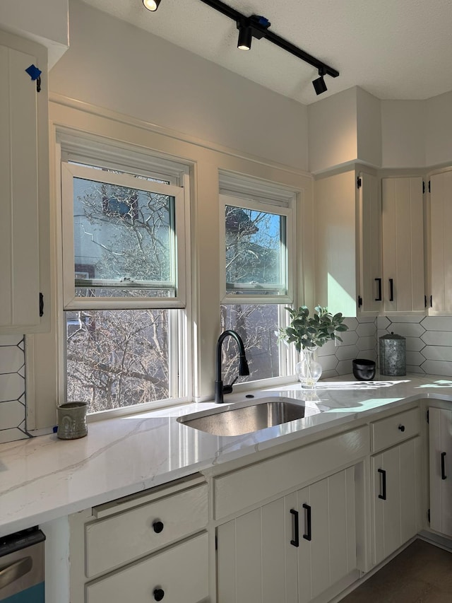 kitchen with light stone counters, tasteful backsplash, white cabinetry, a sink, and dishwasher