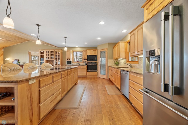 kitchen featuring light wood-style flooring, a sink, light brown cabinetry, a large island, and black appliances