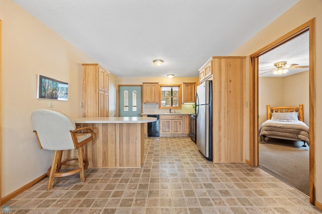 kitchen with a breakfast bar area, a peninsula, light countertops, black appliances, and a sink