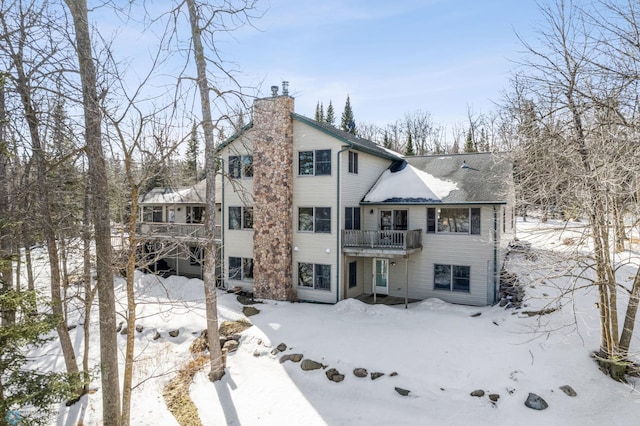 snow covered rear of property featuring a garage and a chimney