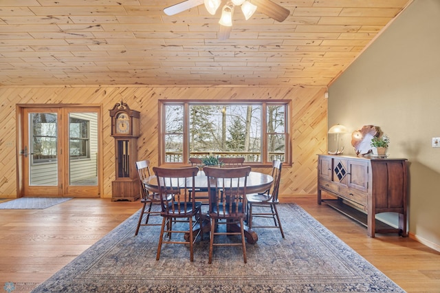 dining space with a ceiling fan, vaulted ceiling, wooden walls, wood finished floors, and wooden ceiling