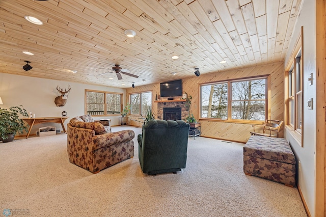 living room featuring wooden walls, visible vents, wooden ceiling, a stone fireplace, and carpet floors