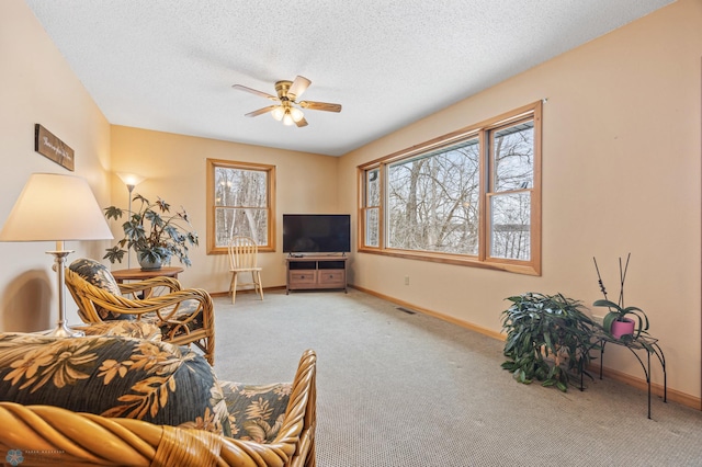 living area with carpet floors, ceiling fan, baseboards, and a textured ceiling