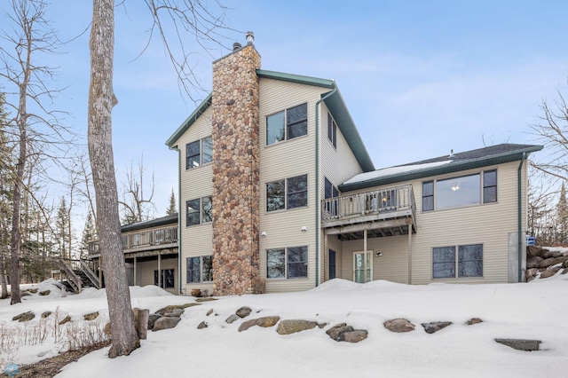 snow covered rear of property featuring a deck, a chimney, and a garage