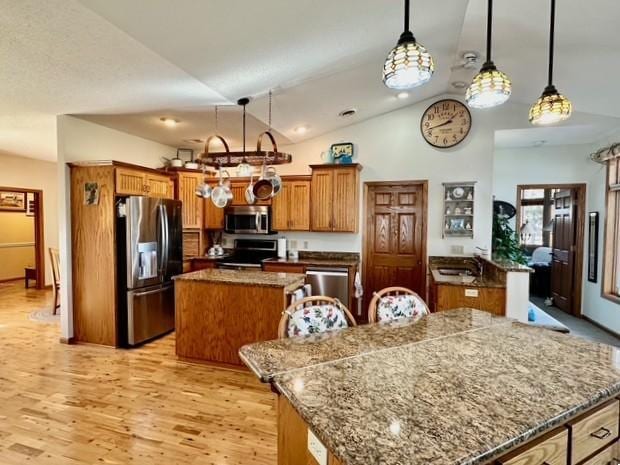 kitchen with brown cabinetry, lofted ceiling, a center island, stainless steel appliances, and light wood-type flooring