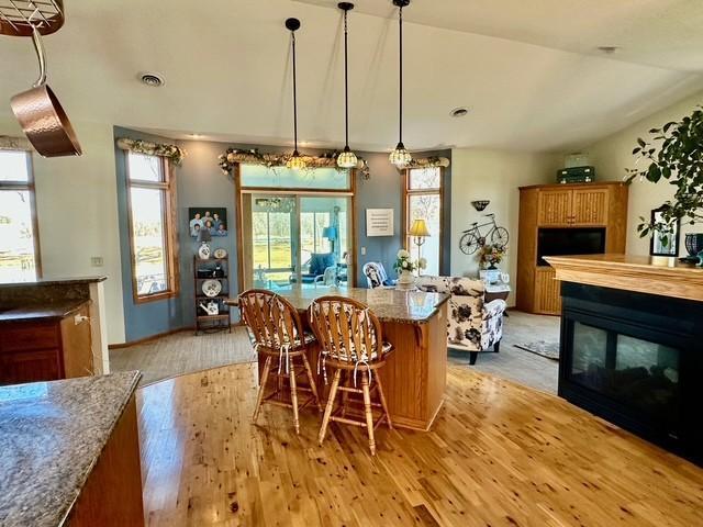 kitchen featuring visible vents, lofted ceiling, light wood-style flooring, a kitchen breakfast bar, and a multi sided fireplace