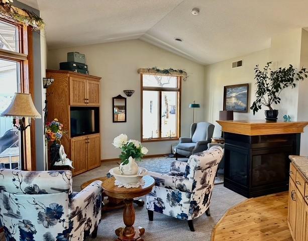 living area featuring a healthy amount of sunlight, visible vents, vaulted ceiling, and a glass covered fireplace