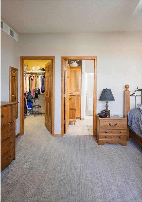 bedroom with a closet, visible vents, light colored carpet, a spacious closet, and a textured ceiling